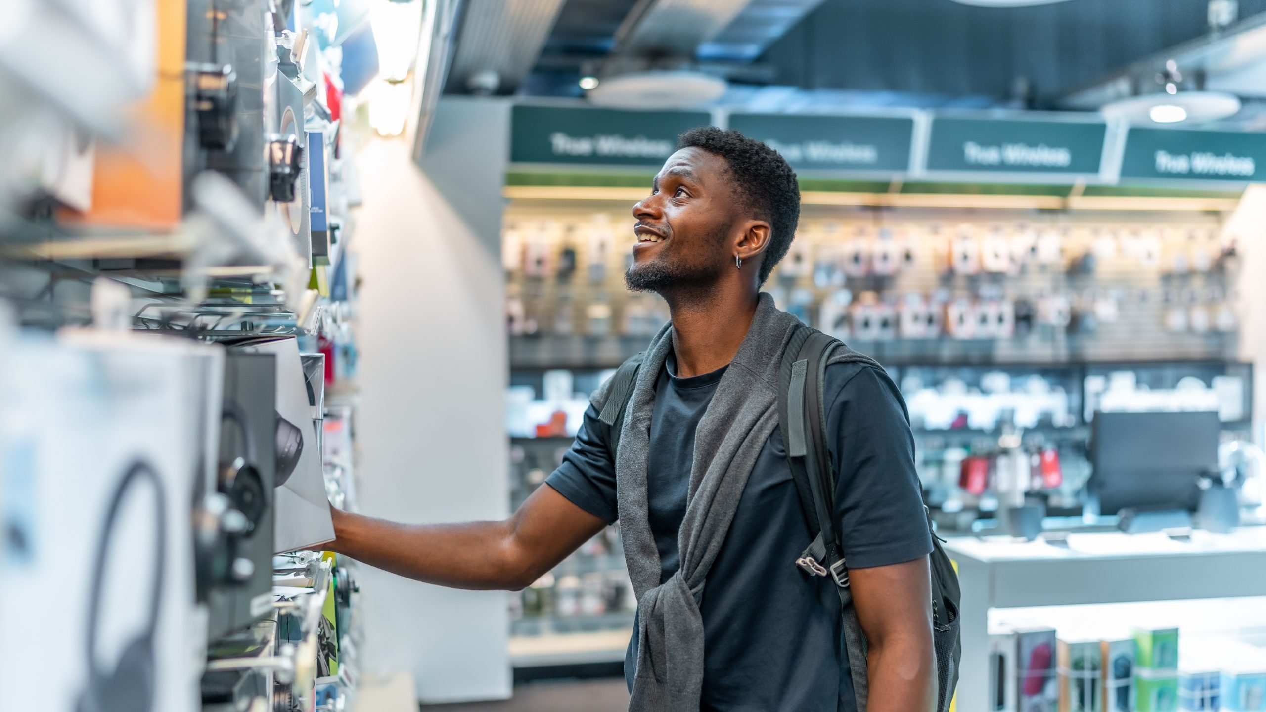 Smiling shopper browsing headphones in an electronics store, for a blog on why customers leave loyalty programmes
